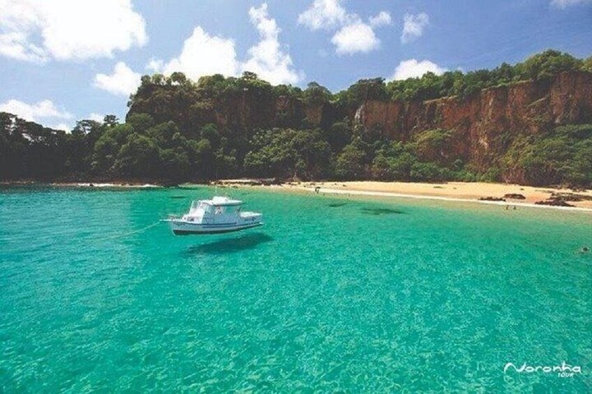 A boat on turquoise water, a sandy beach, and a forested cliff. 4