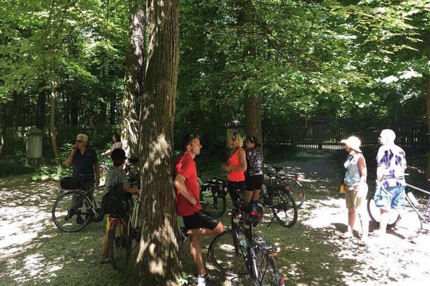 A group of people on bicycles in a park with trees and a fence in the background. 1