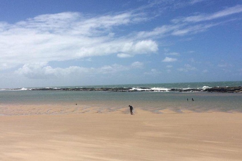 A sandy beach with waves, a clear sky, and a few people. 2