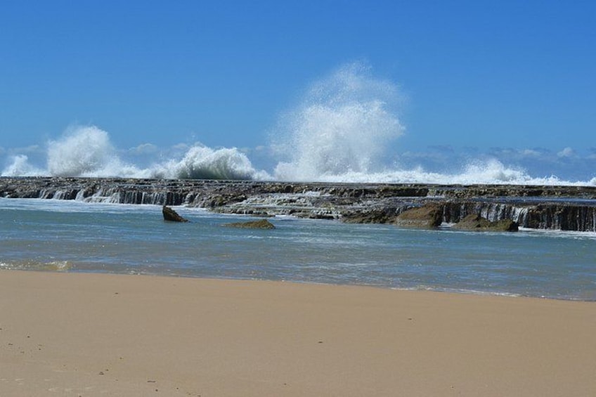 A beach with waves crashing against rocks and a clear blue sky. 4