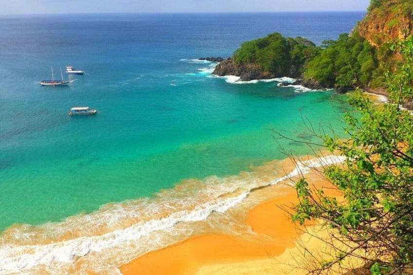 A coastal landscape with clear turquoise waters, a sandy beach, and boats anchored near the shore. 1