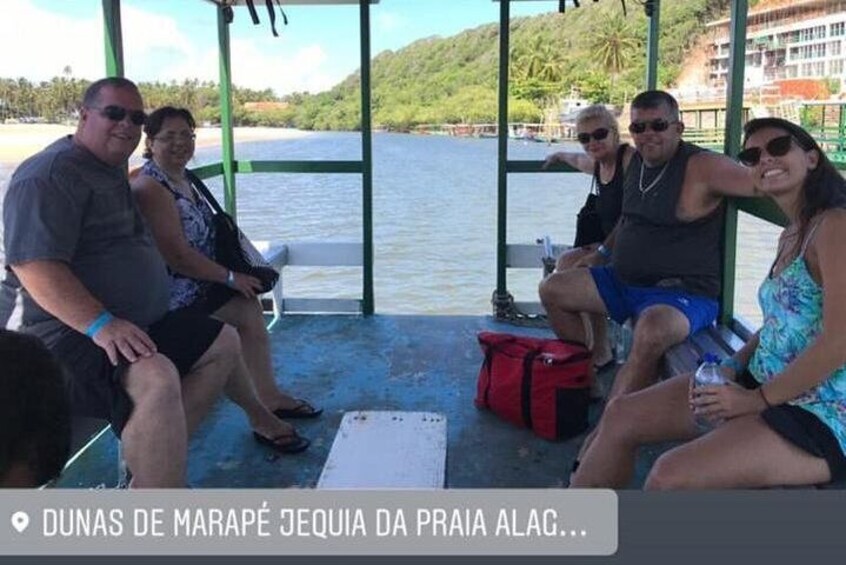 A group of people sitting on a covered deck by a body of water. 3