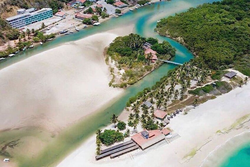 An aerial view of a coastal area with a beach, a small island with buildings, and a bridge connecting to the mainland. 1