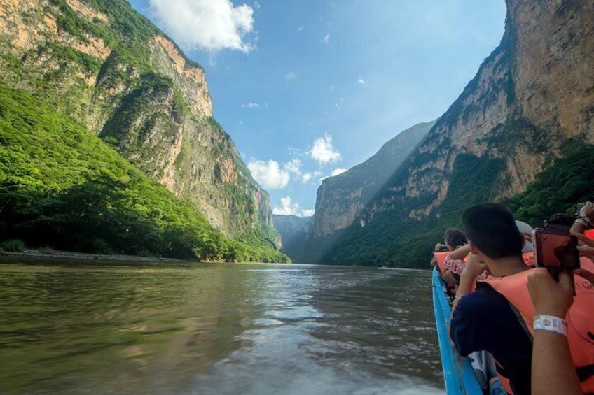A river with steep cliffs on both sides, a boat with passengers, and a clear sky. 1