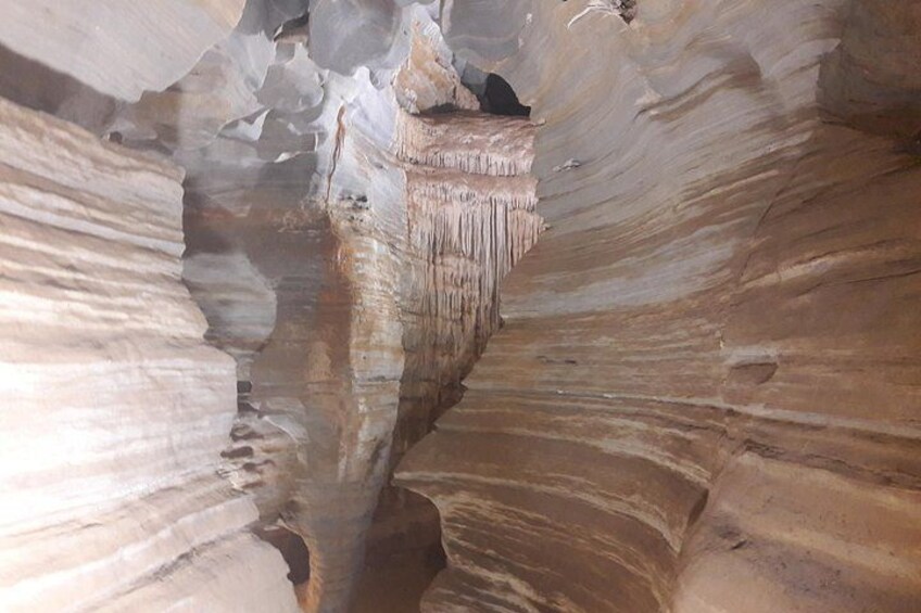 A narrow canyon with smooth, layered rock formations and a small pool of water at the bottom. 3