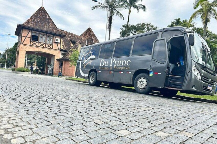 A Du Prime tour bus parked in front of a building with a distinctive architectural style. 2