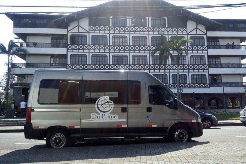 A beige van parked on a paved area with a building featuring a distinctive architectural design in the background. 4