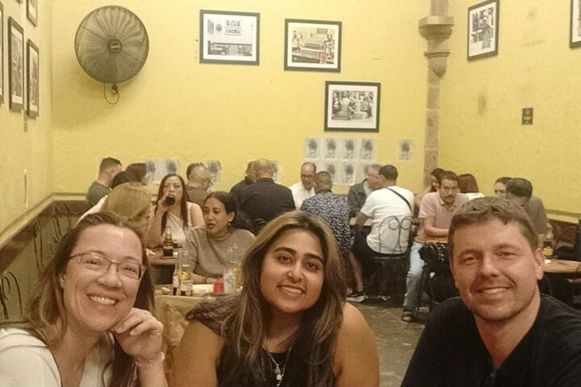 Un groupe de personnes est assis à des tables dans un restaurant aux murs jaunes, et des tableaux encadrés ornent les murs. 3
