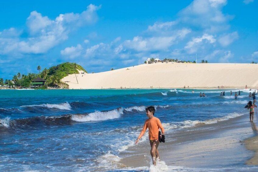 Une plage où l’on voit des gens se promener le long du rivage, des vagues qui se brisent sur le sable et un ciel bleu dégagé. 4