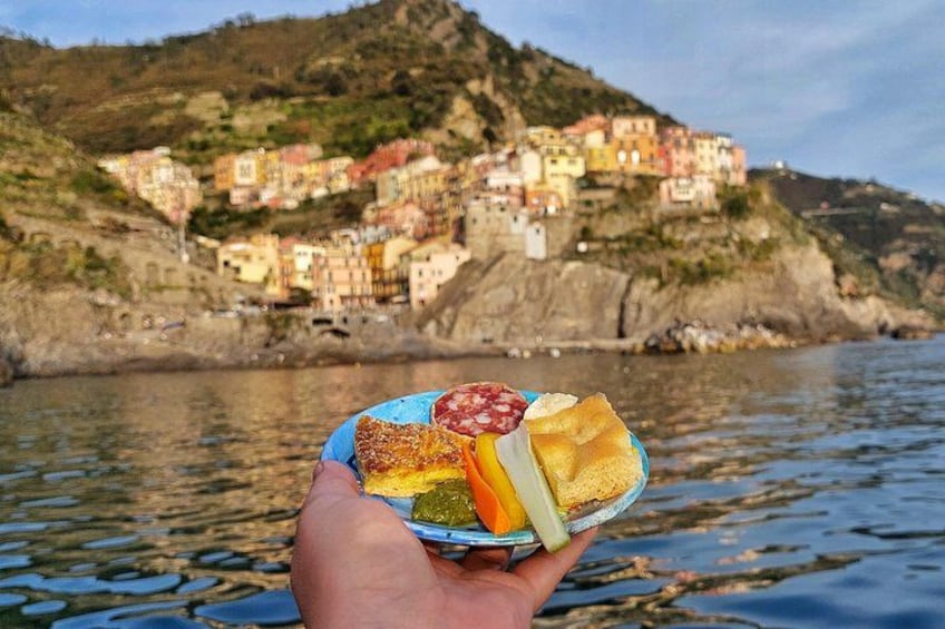A hand holding a plate with food, a coastal town with colorful buildings, and a body of water. 2