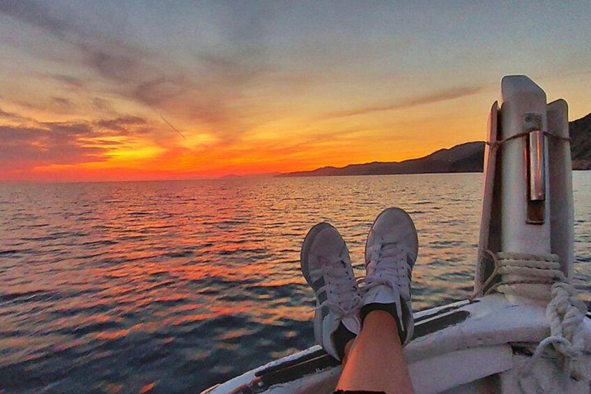 A sunset over a body of water with a boat's railing and a person's feet resting on it. 4
