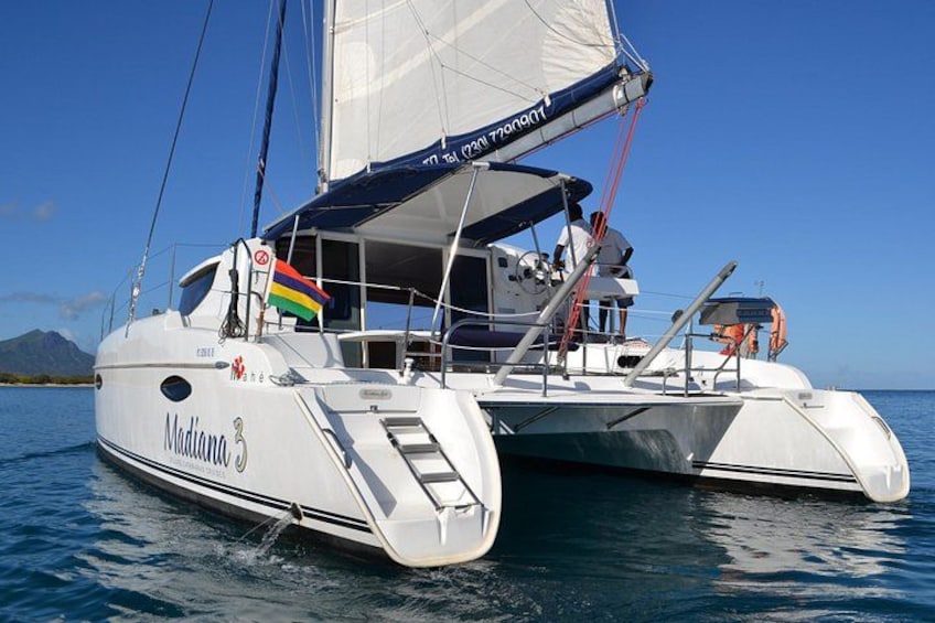 Un trimarán blanco llamado 'Madiana' con una bandera, velas y una persona en la cubierta. 3
