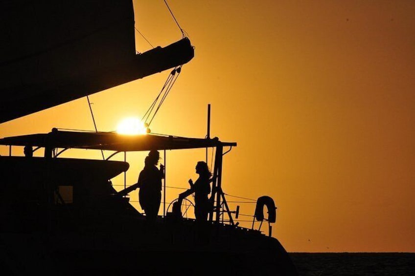 A silhouette of a sailboat with people on deck during sunset. 2