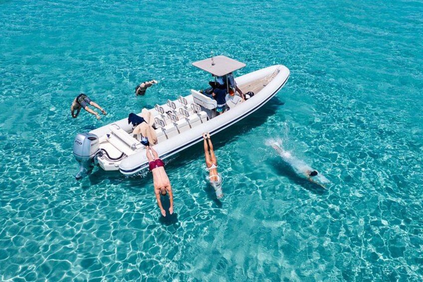 Ein Boot mit darin schwimmenden und schnorchelnden Personen im klaren, blauen Wasser. 1
