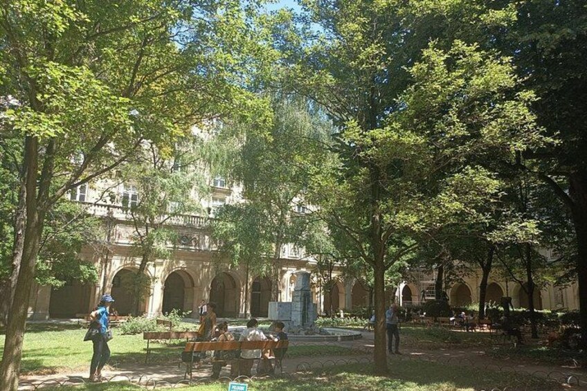 A courtyard with trees, a building with arches, and people sitting on benches. 2