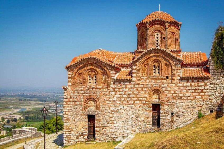 Una iglesia de piedra con tejados de tejas rojas y un campanario. 3