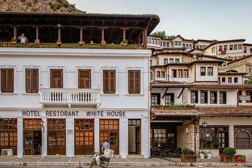 Un edificio blanco con balcón, identificado como 'HOTEL RESTAURANT WHITE HOUSE', y una bicicleta estacionada frente a él. 4