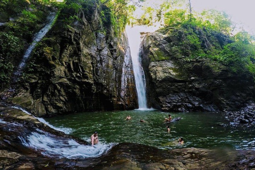 Een waterval, rotsachtig terrein en een zwembad met mensen die zwemmen. 1