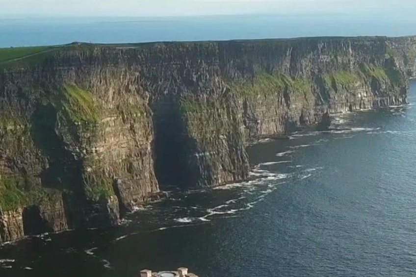 A coastal cliff with a steep drop into the sea, a narrow strip of land, and a clear sky. 1