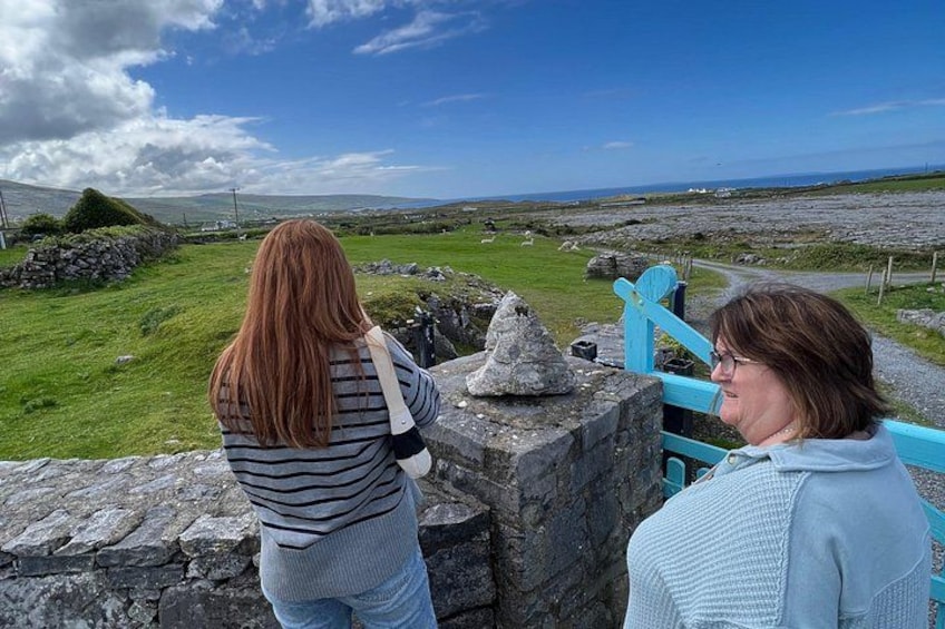 Two people standing by a stone wall with a view of a grassy landscape and a stone structure. 3