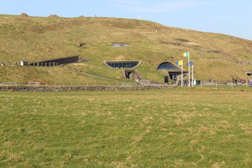 A grassy field with a modern building and a smaller structure on a hill. 2
