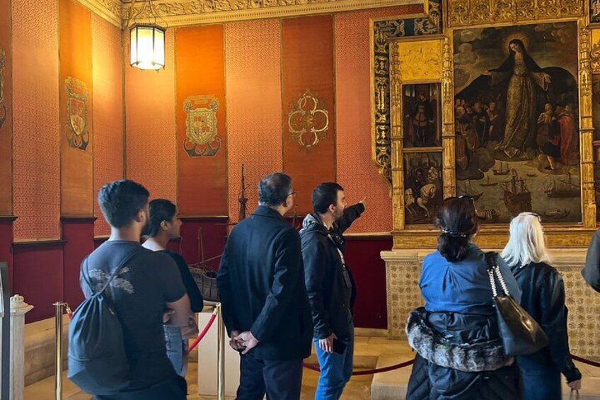 Un groupe de personnes se tient dans une pièce aux murs richement décorés, où est accrochée une grande peinture représentant une figure religieuse. 2