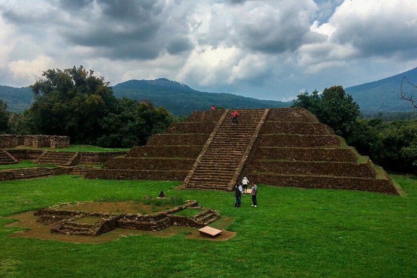 Ancient stepped pyramids, a grassy field, and distant mountains under a cloudy sky. 4