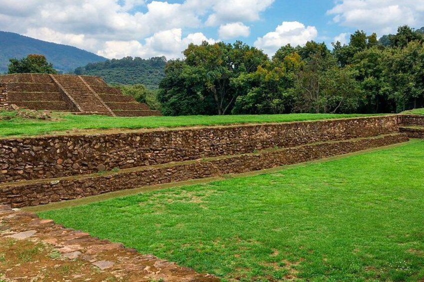 A stone staircase leading up to a pyramid, surrounded by green grass and trees. 3