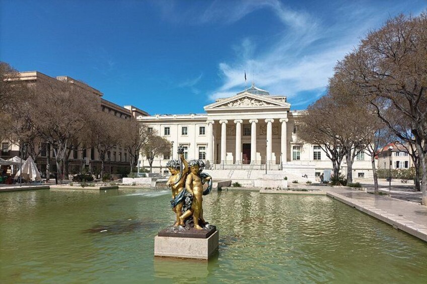 Une statue classique dans une fontaine, un grand bâtiment de style néoclassique et des arbres sans feuilles. 3