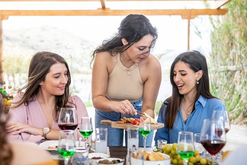 Three people dining outdoors with a table set with wine glasses, plates, and a variety of food. 2