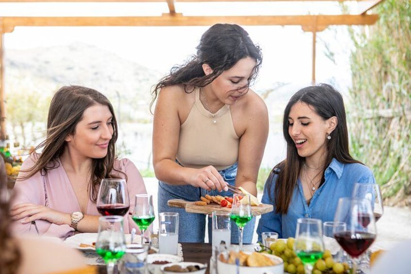 Three people dining outdoors with a table set with wine glasses, a plate of food, and a bottle of wine. 2