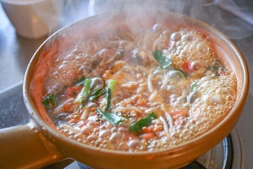 Una olla con sopa hirviendo, fideos, verduras y vapor saliendo. 1