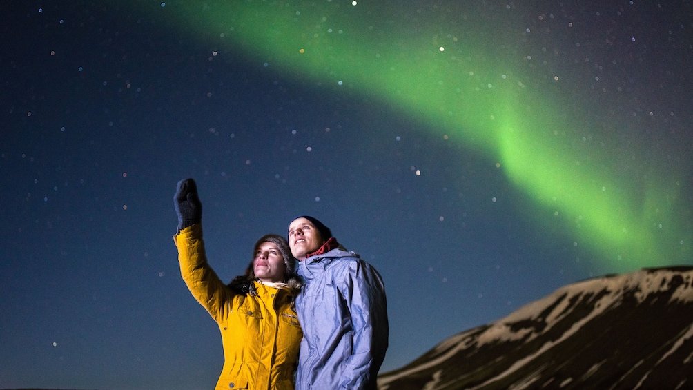 Two people standing under a night sky with the aurora borealis. 5
