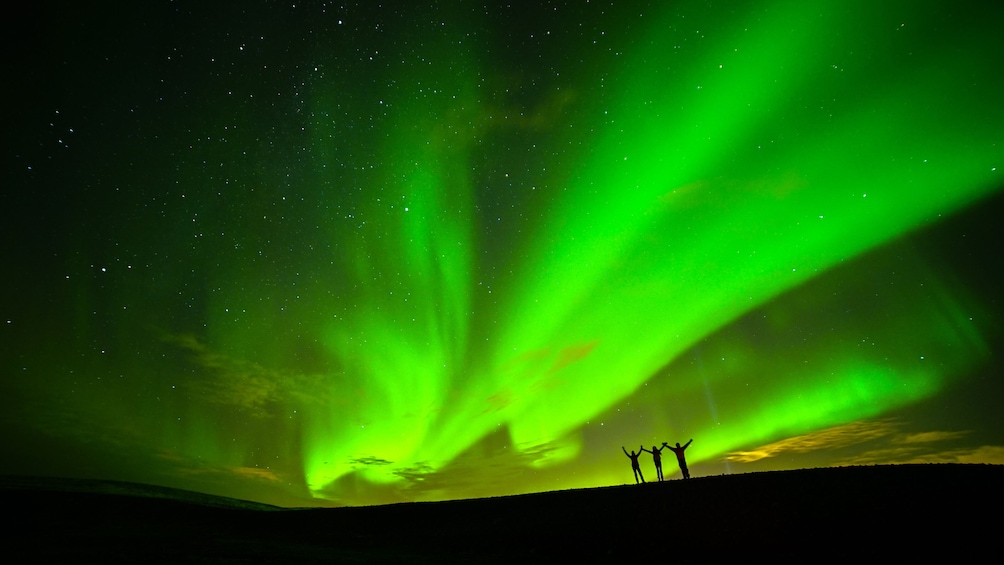 The Northern Lights over a landscape with three silhouetted figures. 4