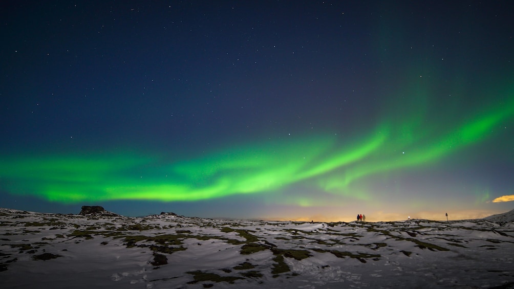 The Northern Lights over a snowy landscape with people observing. 2