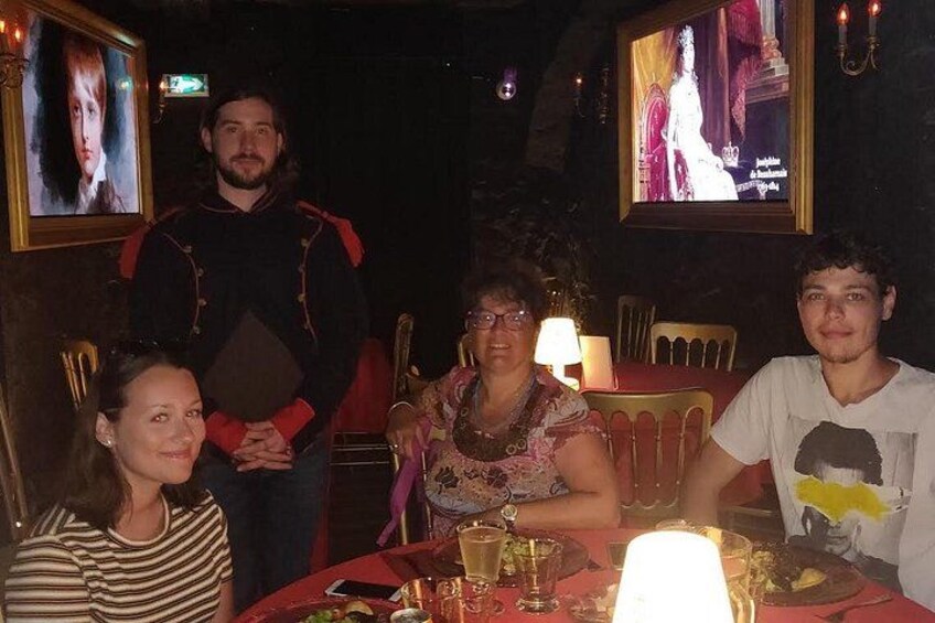 A group of people seated at a table with a lit candle, in a dimly lit room with framed pictures on the wall. 2