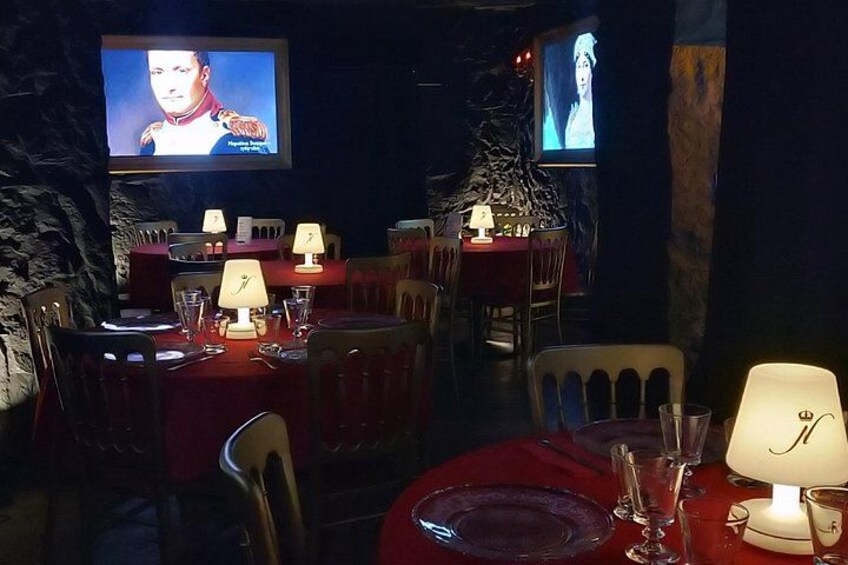 A dimly lit restaurant with tables set for dining, a television screen, and a stone wall. 3