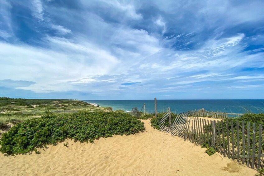 Ein sandiger Strand mit einer Holzlattenzaun, die zum Meer führt, unter einem teilweise bewölkten Himmel. 2