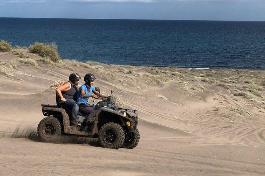 Two people on an ATV on a sandy terrain near a body of water. 2