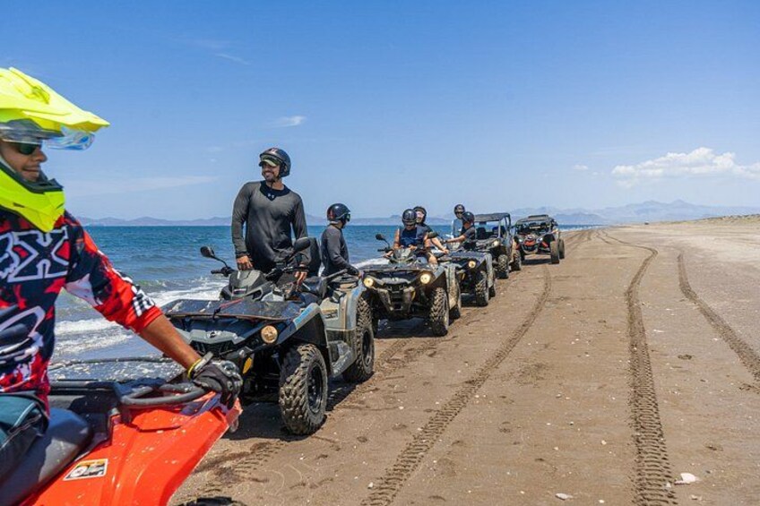A group of people on ATVs on a beach with the ocean and mountains in the background. 4