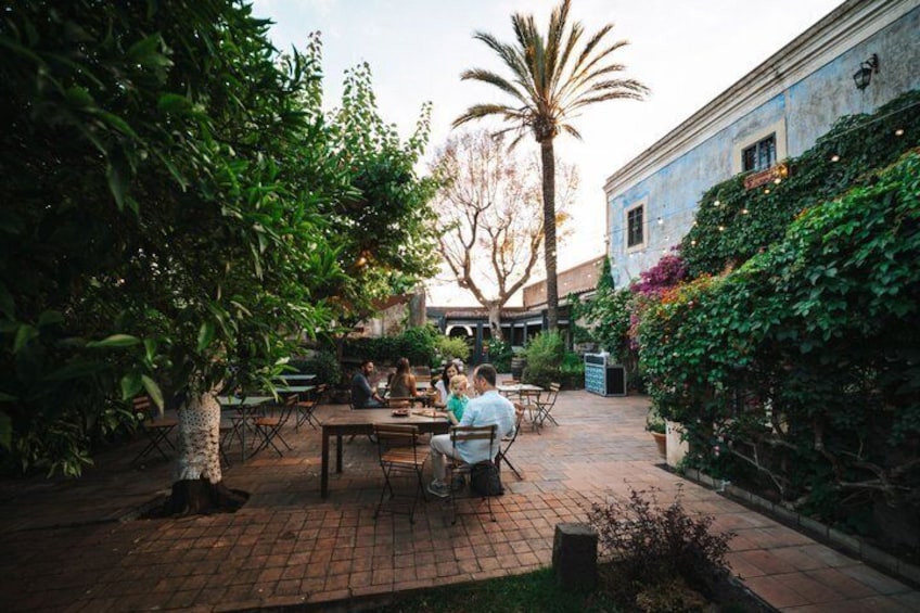 Eine Terrasse im Freien mit Tischen und Stühlen, umgeben von üppiger Vegetation und einer Palme. 2