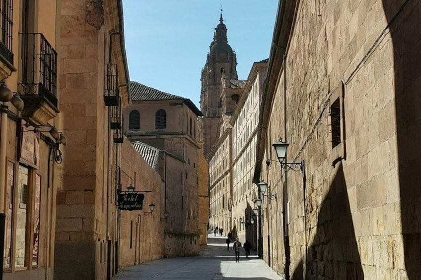 Una stretta via fiancheggiata da edifici storici, insegna di un albergo e campanile di una chiesa in lontananza. 2