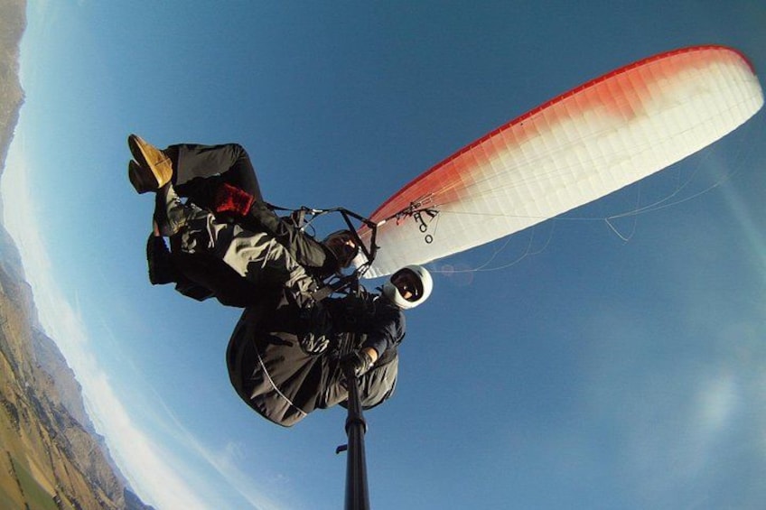 A paraglider in mid-flight with a red and white wing, a clear blue sky, and a mountainous landscape below. 2