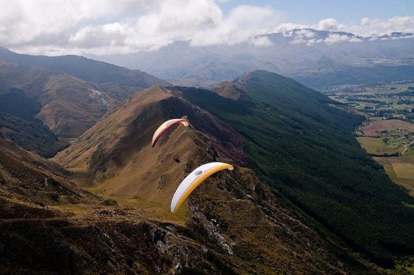 Two paragliders descending over a mountainous landscape. 4