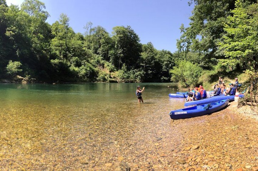 Un groupe de personnes se trouve dans des radeaux bleus sur une rivière aux eaux claires, entourée d’arbres. 1