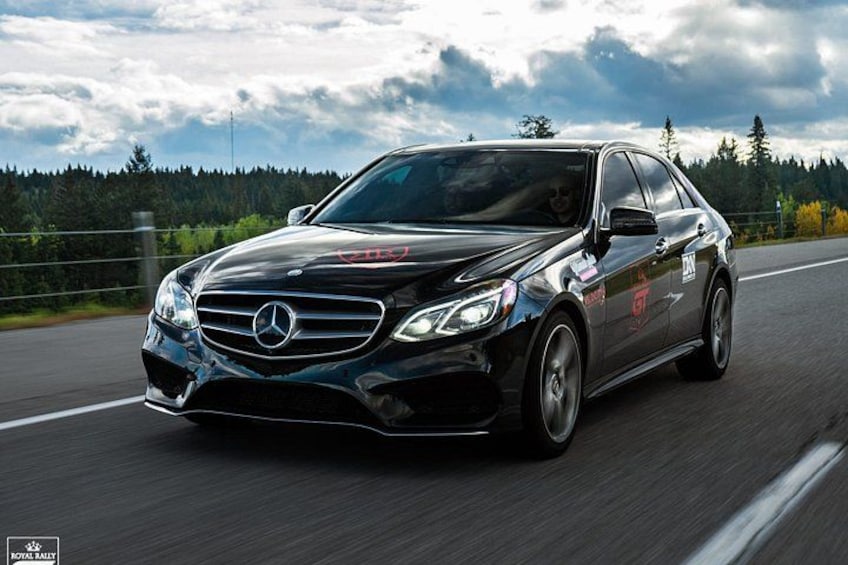 Un coche negro Mercedes-Benz circulando por una carretera con un paisaje boscoso al fondo. 4
