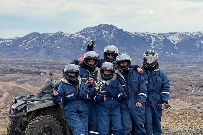 En grupp personer i blå skyddsdräkter och hjälmar poserar tillsammans med ett fyrhjuligt fordon i ett bergigt landskap. 5