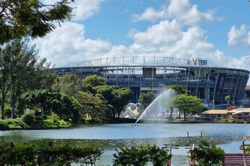 A stadium with a water fountain, surrounded by trees and a lake. 5