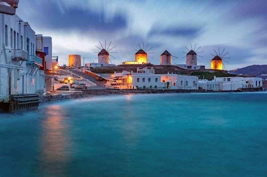 A coastal town with windmills, white buildings, and a calm sea. 5