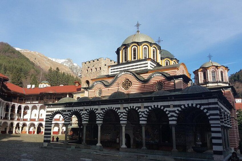 A historic building with a large central dome, arched walkways, and a mountainous backdrop. 5